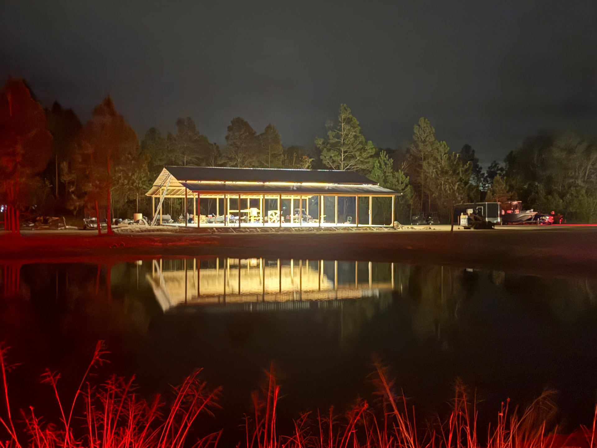 Pole barn outdoor living space lit up at night reflected in a pond